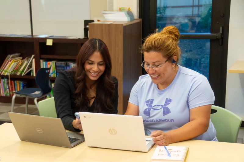 Two women working at their laptops happily